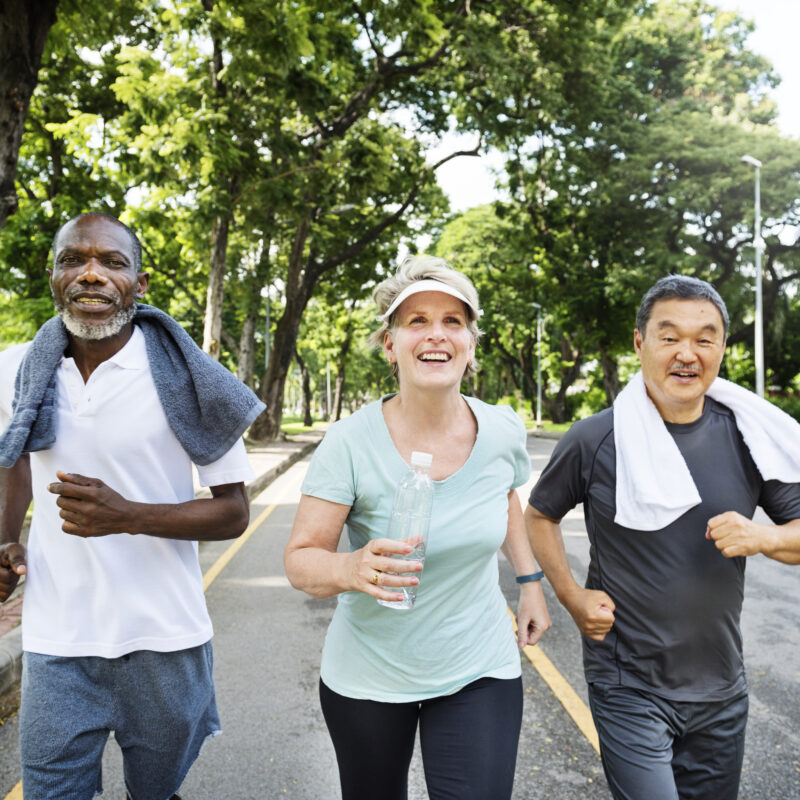 A group of 3 middle aged people are jogging down a neighborhood street.